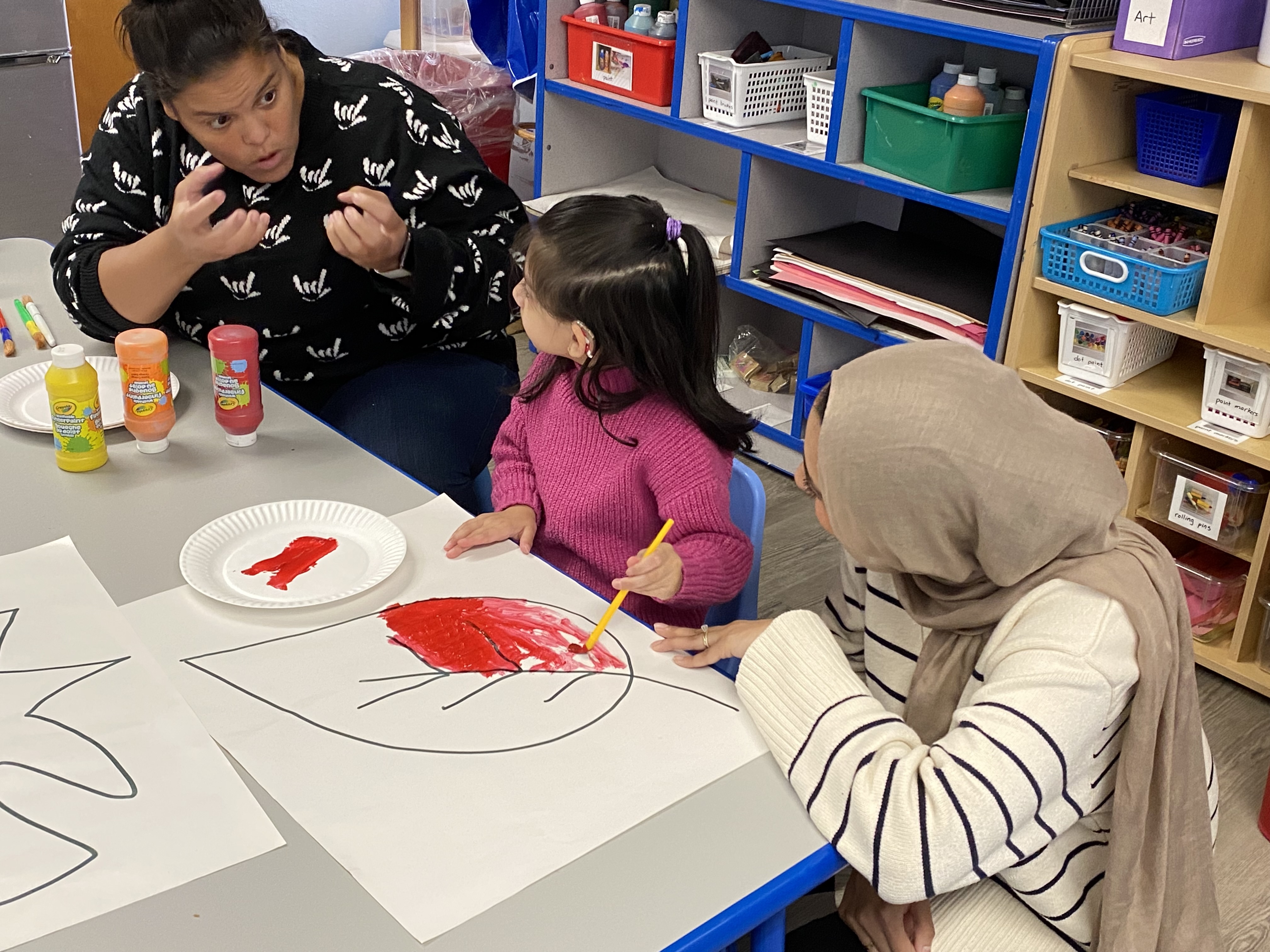 Student painting a picture of a leaf red while looking at teacher asking a question in ASL.